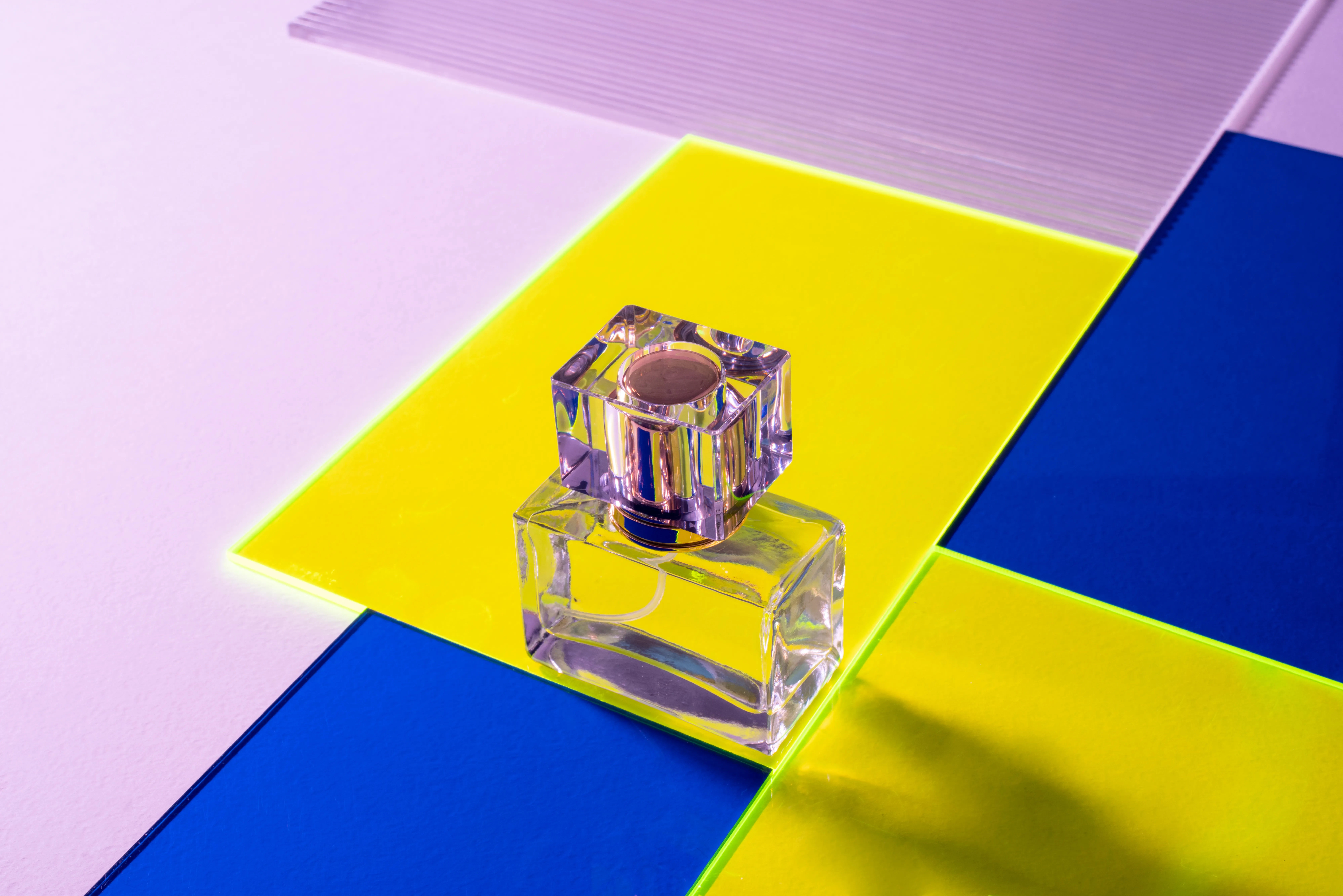 Flacon de parfum transparent sur un fond bleu et jaune symétrique 