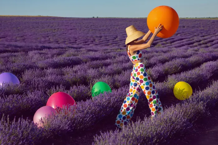 Femme en combinaison d'été à poids colorés qui joue avec des ballons de couleur dans un champs
